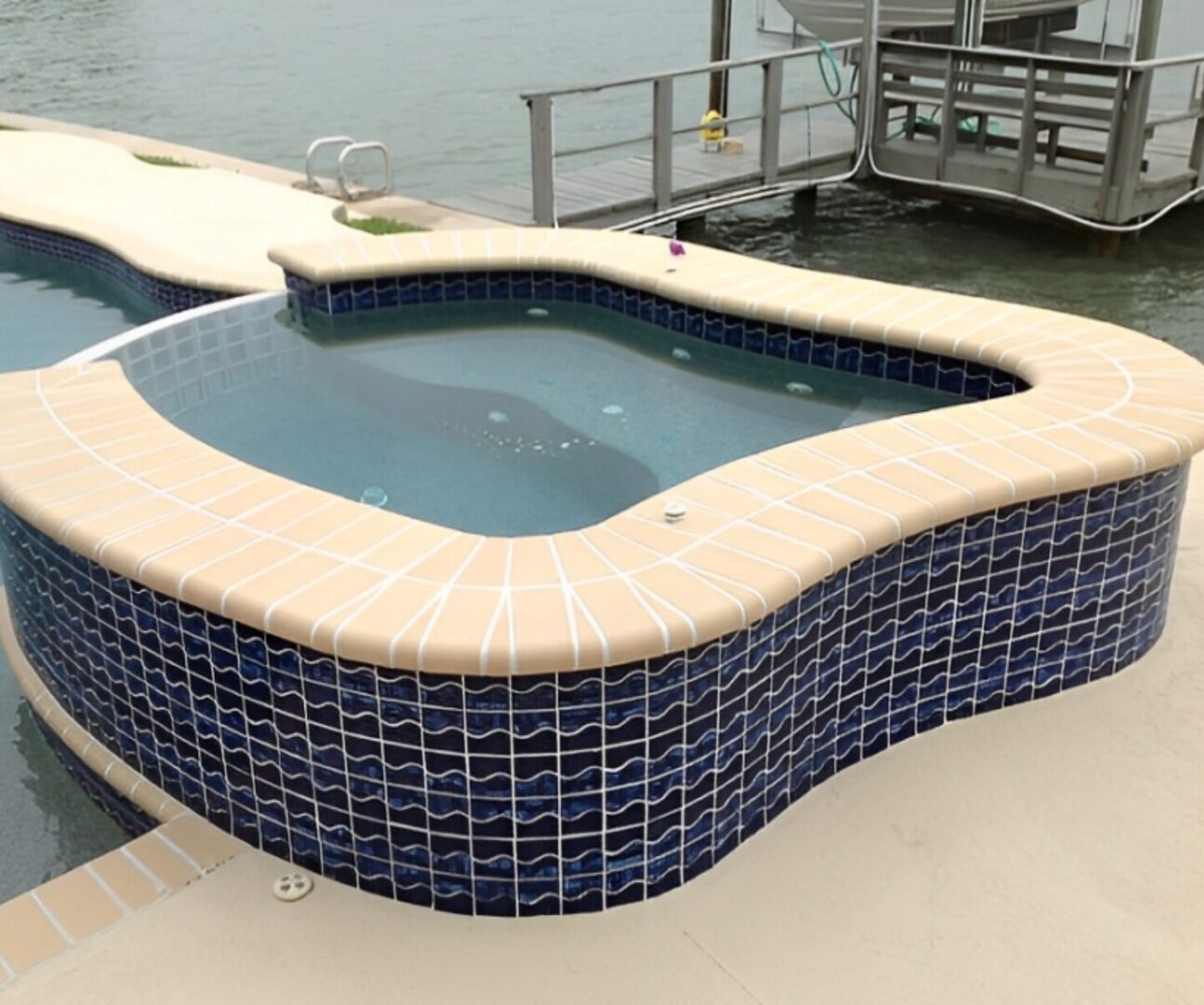 GettyImages-104458435 (1) A small, blue-tiled hot tub is adjacent to a larger pool, both overlooking a body of water.